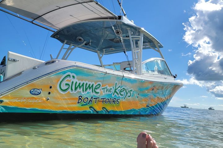 Person's feet in water with a colorful boat and blue sky.